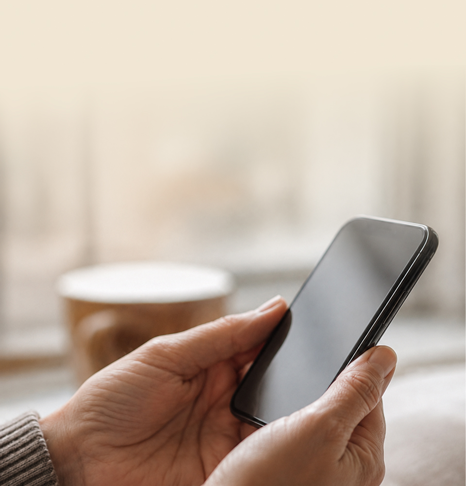 Hands holding a phone, a coffee cup blurred behind